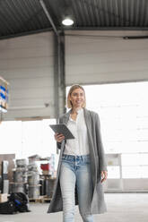 Lächelnde junge Frau mit Tablet in der Hand beim Gang durch eine Fabrik - DIGF09910