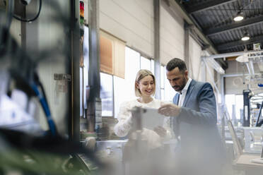 Businessman and young woman with papers talking at a machine in a factory - DIGF09941