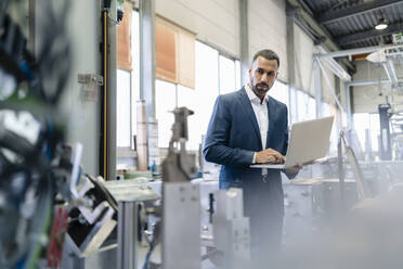 Geschäftsmann mit Laptop in einer Fabrik - DIGF09946