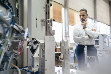 Businessman looking at modern machine in a factory - DIGF09948