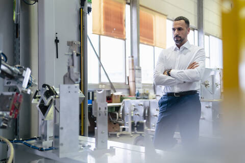 Geschäftsmann vor einer modernen Maschine in einer Fabrik, lizenzfreies Stockfoto