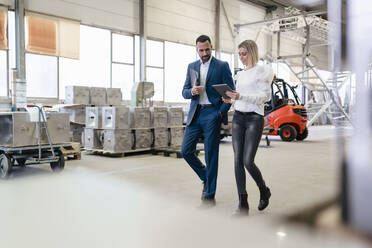 Businessman and young woman with tablet walking and talking in a factory - DIGF09950