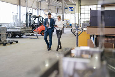 Businessman and young woman with tablet walking and talking in a factory - DIGF09951