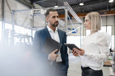 Businessman and young woman with tablet talking in a factory - DIGF09952