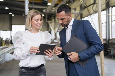 Geschäftsmann und junge Frau mit Tablet im Gespräch in einer Fabrik - DIGF09956