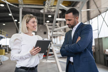 Businessman and young woman with tablet talking in a factory - DIGF09960