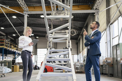Geschäftsmann und junge Frau mit Tablet im Gespräch in einer Fabrik, lizenzfreies Stockfoto