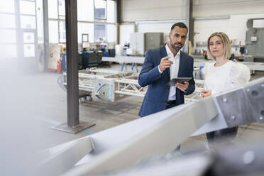 Businessman and young woman talking in a factory - DIGF09965