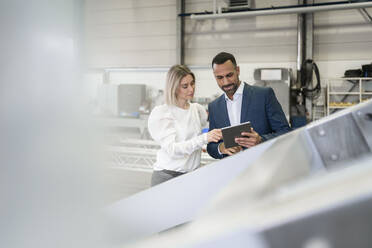 Businessman with tablet and young woman talking in a factory - DIGF09966