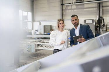 Portrait of businessman with tablet and young woman in a factory - DIGF09967