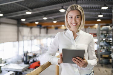 Portrait of smiling young woman using tablet in a factory - DIGF09980