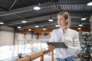 Smiling young woman using tablet in a factory - DIGF09981