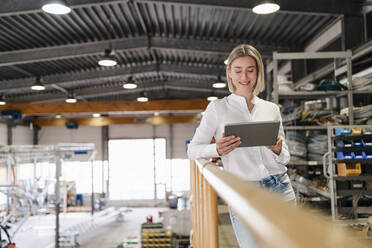 Smiling young woman using tablet in a factory - DIGF09983