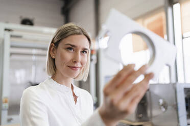 Smiling young woman holding workpiece in a factory - DIGF09987