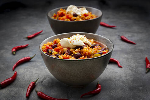 Red chili peppers and two bowls of vegetarian chili with red lentils, kidney beans, tomatoes, carrots, celery and sour cream - LVF08855