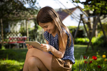 Glückliches Mädchen sitzt im Garten und benutzt ein digitales Tablet - LVF08861