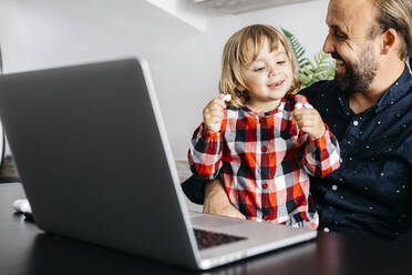 Happy father with daughter having a video chat at desk - JRFF04381