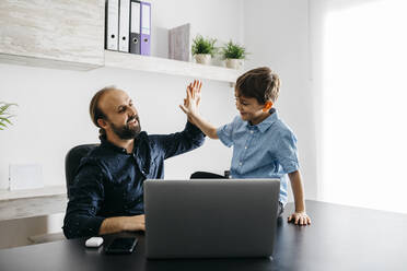 Happy father high fiving with son at desk - JRFF04384