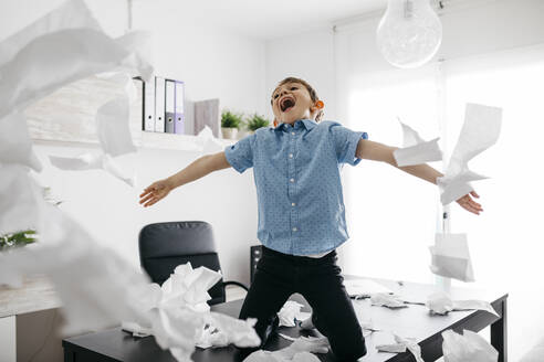 Schelmischer Junge spielt mit Toilettenpapier auf dem Schreibtisch im Büro zu Hause - JRFF04393
