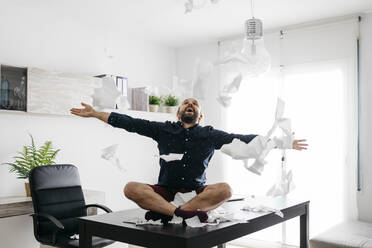 Mischievous boy playing with toilet paper on desk in home office - JRFF04396