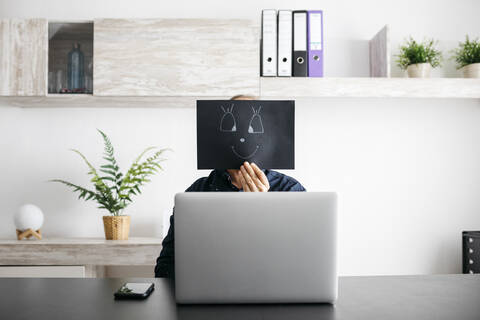 Mann arbeitet zu Hause mit einer schwarzen Pappe im Gesicht, lizenzfreies Stockfoto