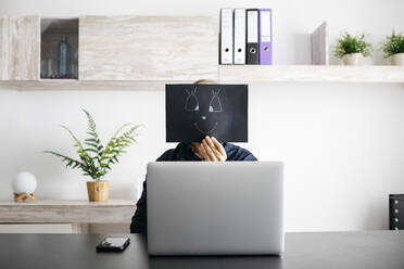 Man working at home with a black cardboard covering his face - JRFF04397