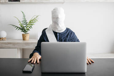 Man working at home with his head covered in toilet paper - JRFF04399