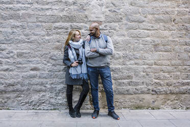 Happy couple standing in front of stone wall looking at each other - XLGF00091