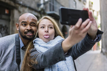 Porträt eines Paares, das sich bei der Aufnahme eines Selfies mit einem Smartphone die Gesichter verzieht, Barcelona, Spanien - XLGF00103