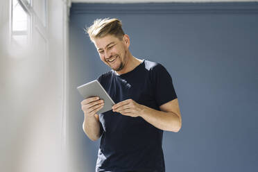 Happy man using a tablet at the window - JOSEF00509