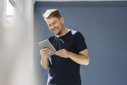 Fröhlicher Mann, der ein Tablet am Fenster benutzt - JOSEF00509