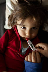 Porträt eines kranken Mädchens auf der Couch mit digitalem Thermometer, in den Händen der Mutter - VABF02821