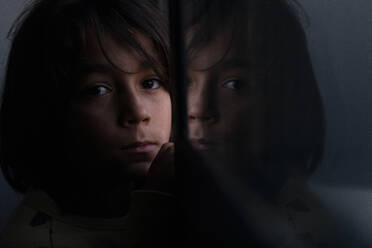 Junge blickt in die Kamera, die sich in einer Fensterscheibe zu Hause spiegelt - VABF02831
