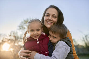 Porträt einer glücklichen Mutter, die zwei Kinder im Freien umarmt - ZEDF03343