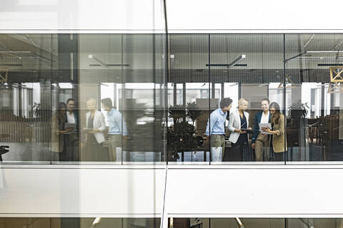 Geschäftsfrau und Angestellte unterhalten sich hinter einer Fensterscheibe im Büro, lizenzfreies Stockfoto