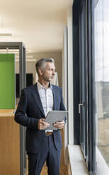 Älterer Geschäftsmann mit Tablet im Büro und Blick aus dem Fenster - PESF01981