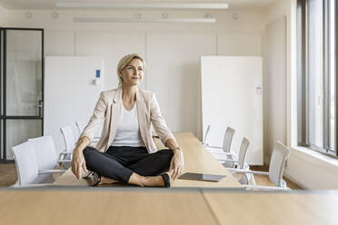 Blonde Geschäftsfrau sitzt auf einem Tisch im Konferenzraum - PESF02001