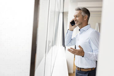 Mature businessman talking on the phone at the window in office - PESF02003