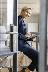 Porträt einer lächelnden blonden Geschäftsfrau, die in einem Konferenzraum ein Tablet benutzt - PESF02013