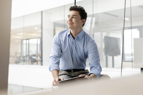 Porträt eines lächelnden jungen Geschäftsmannes mit Tablet am Fenster im Büro - PESF02033