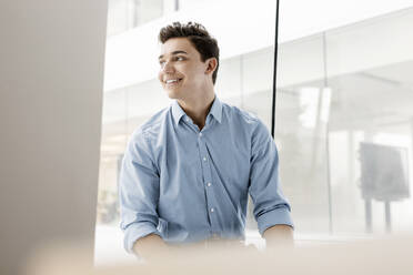 Portrait of smiling young businessman at the window in office - PESF02036