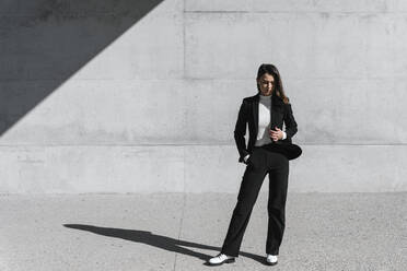 Young woman wearing black suit standing in front of concrete wall - TCEF00524