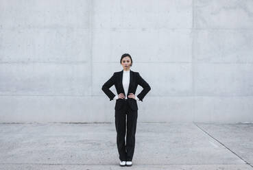 Young woman wearing black suit standing in front of concrete wall - TCEF00528