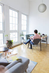 Man sitting at table at home looking at photographs - FKF03725