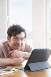 Portrait of smiling man using tablet on table at home - FKF03735