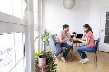 Couple sitting at table at home talking - FKF03741