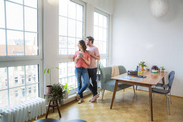 Couple standing at the window at home looking out - FKF03744