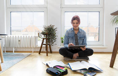 Teeange girl sitting on the floor at home learning - FKF03751