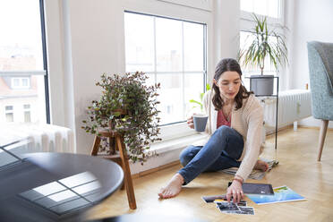 Woman sitting on the floor at home looking at photographs - FKF03758