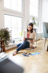 Woman sitting on the floor at home looking at photographs - FKF03759